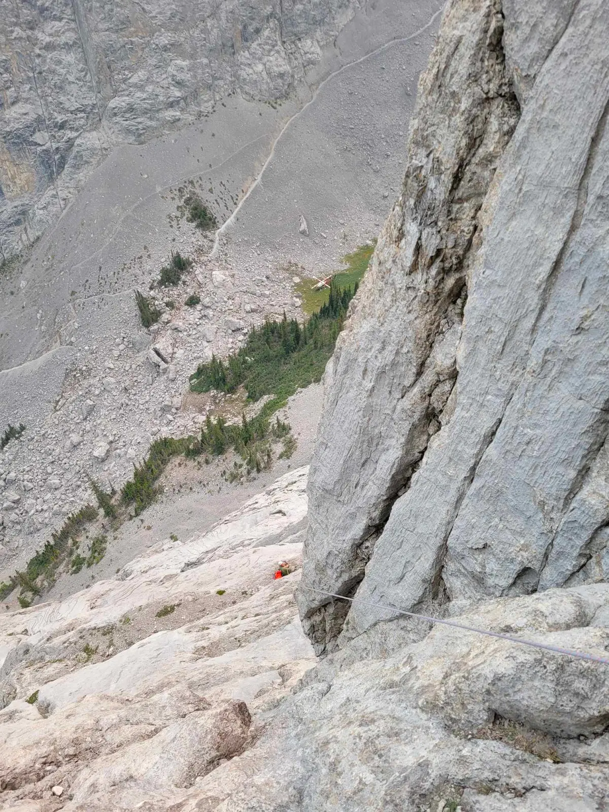 Alistair's photo of me on the ledge upon reaching the anchor that I fell from. I am connected to the blue rope. The rescue helicopter can be see in the valley floor far below, staging for the rescue.